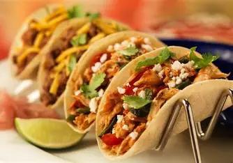 Closeup photo of several chicken or beef tacos sitting in a metal divider that is holding them upright and keeping their fillings from falling out. 