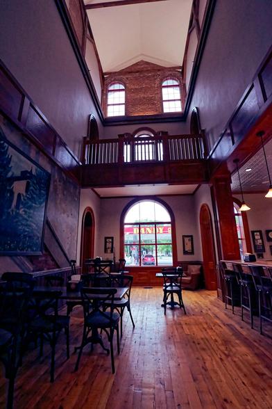 Tall room with an upstairs balcony, wood floors,  many chairs and a sign that says DANDY seen through a big window