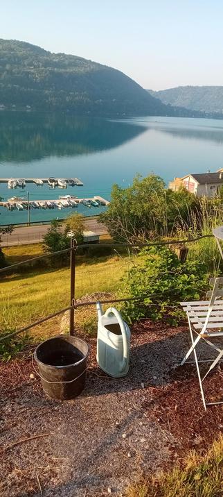 Une vue sur un lac.  Au premier plan: un seau, un arrosoir, une chaise et un bout de  table
