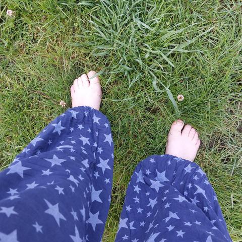 A pair of legs with blue star print baggy trousers and bare feet sticking out the bottom on grass.