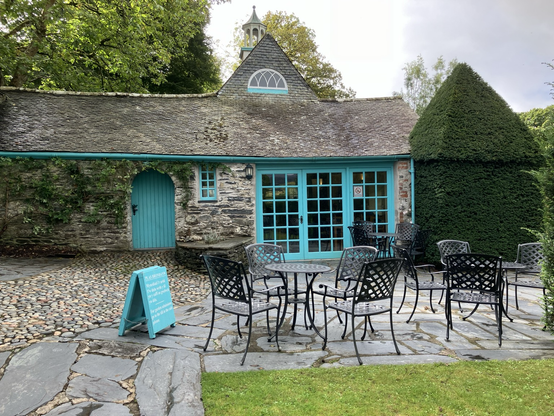 A grey granite building with a beautiful grey slate roof, with bright turquoise paintwork on windows, French doors and a gate. 