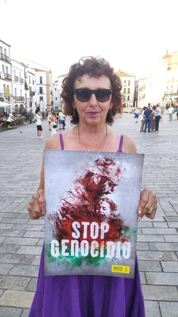 Una mujer, en la Plaza Mayor de Cáceres, sosteniendo un cartel con el lema STOP GENOCIDIO.