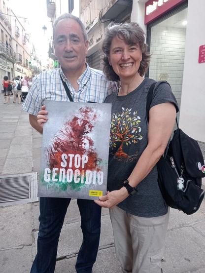Un hombre y una mujer sosteniendo un cartel con el lema STOP GENOCIDIO.