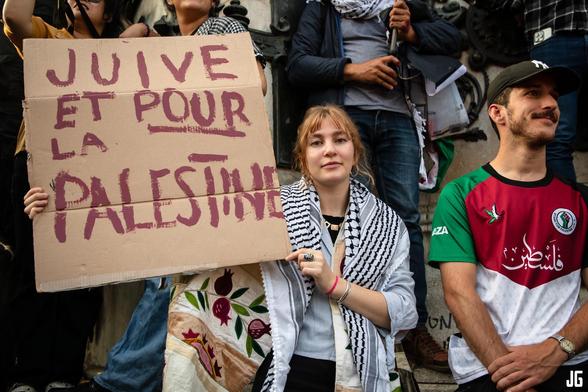 Au pied de la statue, une manifestante portant un keffieh sur les épaules brandit une pancarte où l’on peut lire : « Juive et pour la Palestine ».