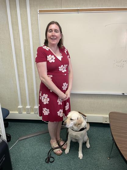 Photo of Lindsey with her guide dog Winona standing in a classroom.