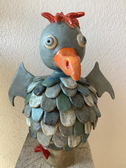 Blaugraue Keramikfigur mit großem Schnabel (orange), rotem gezacktem Schwanz und kleine Flügeln.