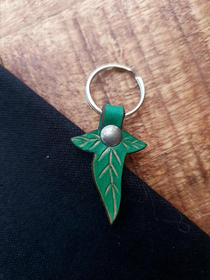 Leather green Lorien leaf keychain on a black and wood background