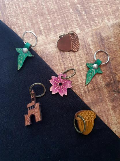 Leather keychains on a black and wood background: a castle, a sakura (cherry blossom), an acorn and a Lorien leaf 