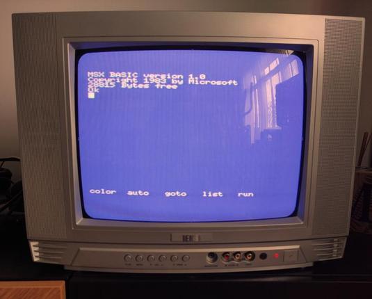 Foto de un televisor CRT mostrando la pantalla principal de un MSX Canon V-20 en el que se puede leer MSX BASIC version 1.0 Copyright 1983 by Microsoft