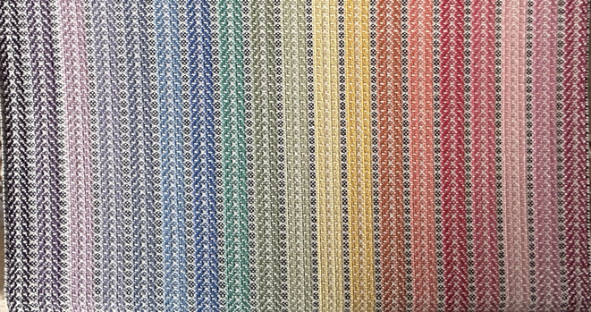 A handwoven length of twisted twill fabric on a handloom in a rainbow range of colours