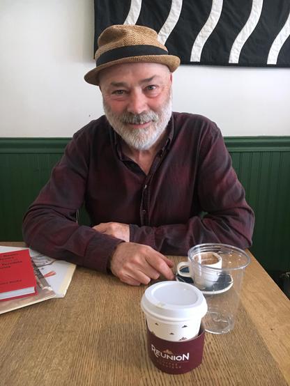 A man wearing a hat sits at a table, enjoying a cup of coffee.