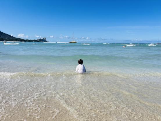 Small boy sitting on the beach, facing the waves
