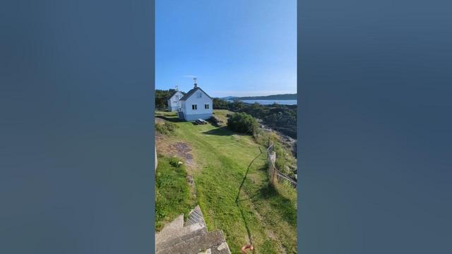 a door opens, and you see white houses on a green coast line, and as the camera pans, there are distanced islands and a blue ocean under a near cloudless and sunny sky