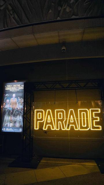 Photo of an advert for 'Parade' along with a yellow neon sign outside of the Ahmanson Theatre, as seen during the musical's opening night in Los Angeles.