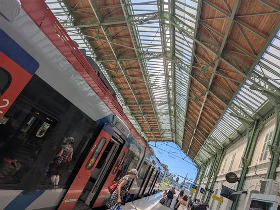 Un TER Regiolis en gare de Evian-les-Bains sous la verrière. Il vient d'arriver en provenance de Bellegarde/Annemasse. Des voyageurs descendent du train. Jour d'été de forte chaleur.