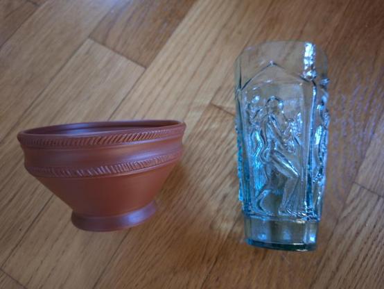 Foto meiner Neuzugänge: Links eine kleine rotbraune Terra-Sigillata-Schale mit Kerbschnitt- oder Rädchenverzierung am (geknickten) Rand, rechts eine Replik eines formgeblasenen römischen Glasbechers mit mythologischen Szenen