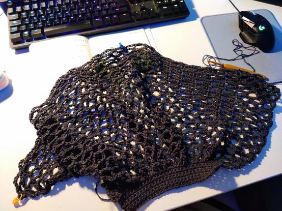 Extendido sobre la mesa una labor de ganchillo a medio tejer. Parece una red o una malla negra, aunque en color real es más bien un gris carbón.