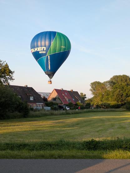 Foto. Heißluftballon schwebt dicht über den Dächern einer kleinen Siedlung vorüber. 
