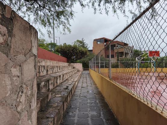 Un pasillo mojado de lluvia entre las canchas y las gradas de un parque municipal