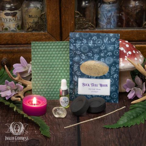 The contents of our exclusive "Buck Full Moon Ritual Kit for the July 12th, 2025, Full Moon in Capricorn" product are arranged on a wood surface. They include a sheet of green beeswax and a wick; a pouch of Buck Full Moon herbs, including bay leaf, thyme, and ginger; a dropper vial of our exclusive Full Moon Spell Oil; a tumbled citrine gemstone; and two charcoal discs. Presented by Inked Goddess Creations.