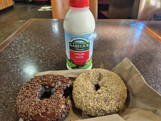 Photo of a double chocolate donut, a butternut donut, and a bottle of milk from Honey Dew Donuts.