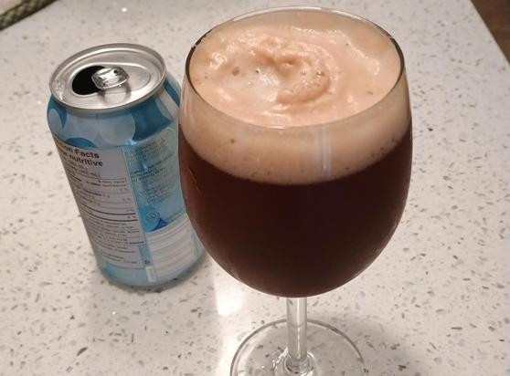 A glass is full of a dark brown liquid with a beige frothy foam on top