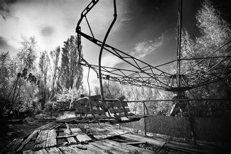 A black & white picture of an overgrown merry-go-round in Prypiat, with some planks missing. Prypiat was a residential town of 50,000 people, servicing Chernobyl.