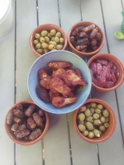 Mehrere Schüsseln mit Oliver, Chicken wings, Salami, Datteln.