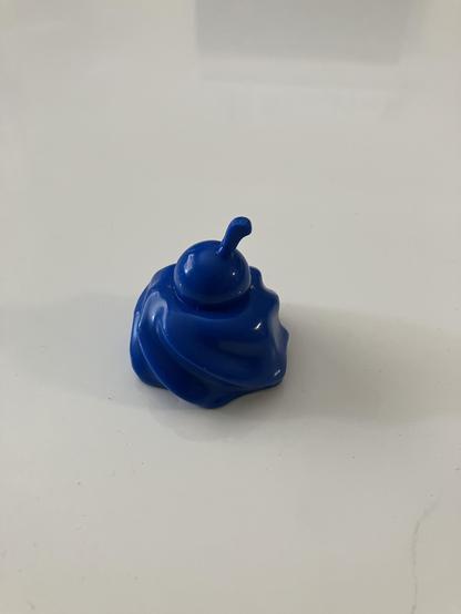 Ein blaues hartes Plastikkteil in form eines Küchleins mit einer Art Kirsche drauf.