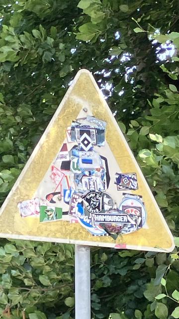 Ein Verkehrsschild, das vor dem Schleudern warnt ist übersäht mit HSV und anderen Aufklebern.