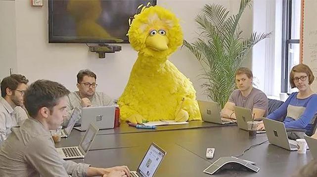 La gallina Caponata, con mirada triste y ausente, sentada en una mesa de reuniones junto a un montón de gente con sus portátiles. 
