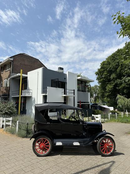 A Ford T in the foreground and a modern white and grey building with black, yellow and red accents in the background: the Rietveld Schröder House in Utrecht.