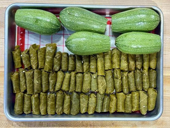 A top down view of a ¼ sheet pan with five squash and over fifty stuffed grape leaves. 