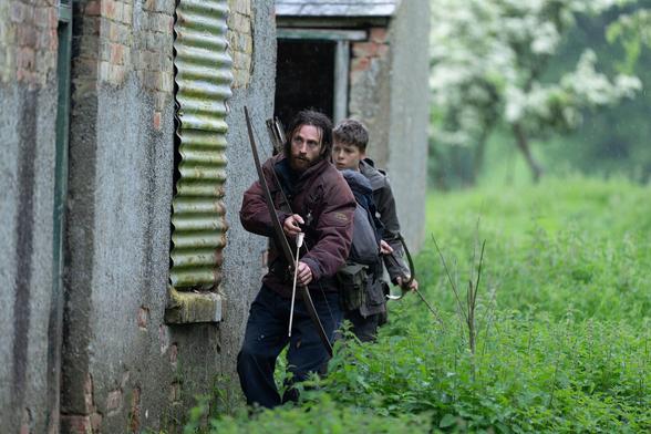 Imagen promocional de la película '28 años después'. Se muestra a dos personajes, un padre y un hijo, armados con arcos y flechas en el lateral de una casa.
