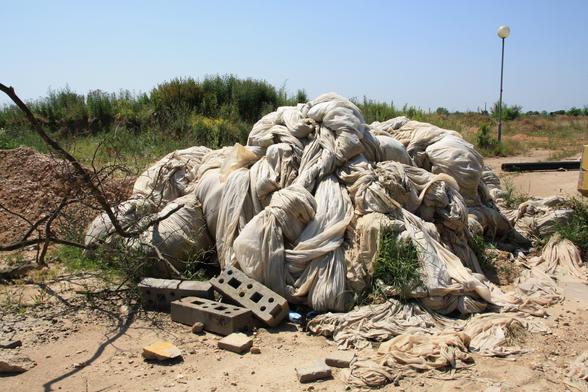 Überbleibsel von Straßenbarrikaden, ein Haufen weißer Folie, der mit zusammengekniffenen Augen aussieht wie ein Haufen toter, weißer Pferde. Dahinter eine Straßenlaterne, die zusammenhanglos im Nichts überwucherten Asphalts steht.