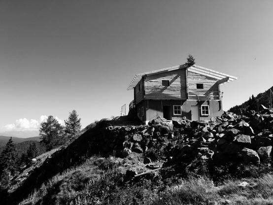 A mountain hut build with stones and wood above a hill in the mountains. The sky is clear