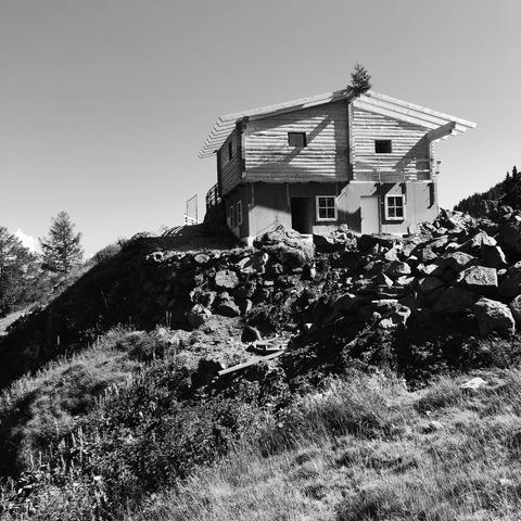 La facciata esposta al sole di una malga di montagna attualmente in fase di ristrutturazione posizionata su una collina. Il cielo è sereno