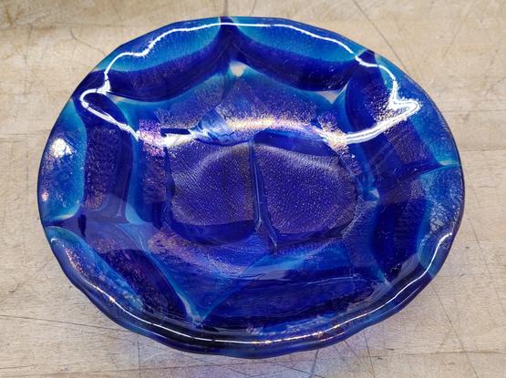 A circular plate of fused glass that was fired again in a mold to make a bowl. It was made from chunks of a pattern bar of layers of blue and clear glass - it is several shades of blue and I am so happy with it. 