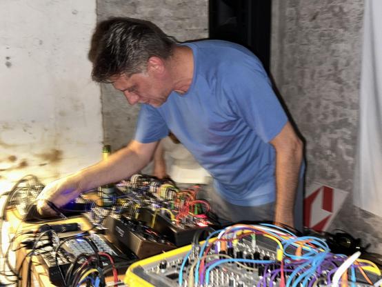 Alexander Spree wearing a sky blue t-shirt as he plays his electronic music instruments including a  Make Noise 0coast synths or 0ctrl sequencer, which was just one piece among many in his setup.