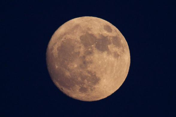 Image of a nearly full Moon against a dark blue sky. This June moon from 9:31 pm EDT on June 9 is just 30 hours short of being completely full. The edges of the left and lower left show the small hint of shadow and definition on the edges of craters where it is not yet completely full.