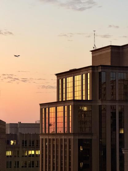 The sunset is reflected in the windows of a building as a plane flies past 