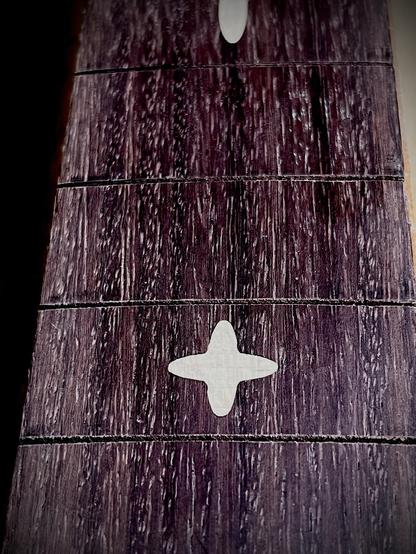 Ein Gitarrengriffbrett aus Palisander mit Ahorn Einlagen, Detailaufnahme von oben. Die Schlitze für die Bundstäbchen sind gesägt, aber noch keine Bünde eingesetzt.
A guitar fretboard made from indian rosewood with maple inlays. Close-up from above. Fretslots are sawed, but the frets are not installed yet.