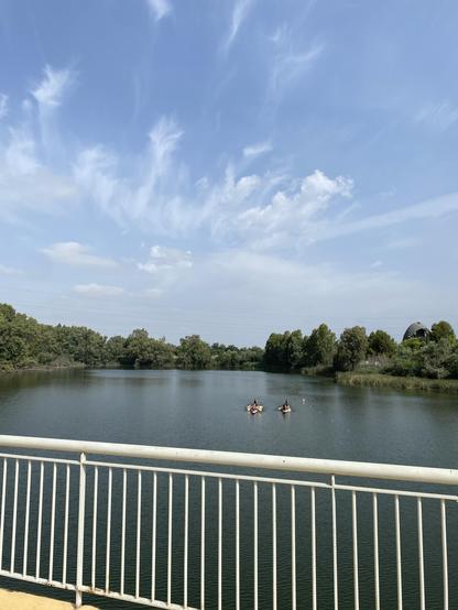 Foto del cielo desde el río Guadalquivir, por la mañana. Se ven algunas pocas nubes de forma alargada. En el río hay dos barquitos de remo. Se ve la vegetación del parque que rodea al río.