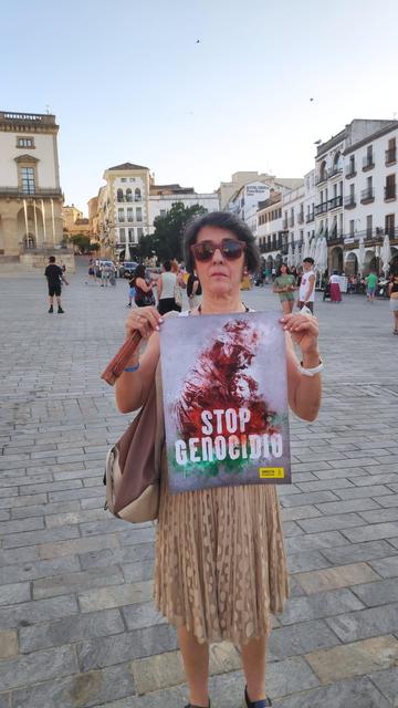 Una mujer, en la Plaza Mayor de Cáceres, sosteniendo un cartel con el lema STOP GENOCIDIO.