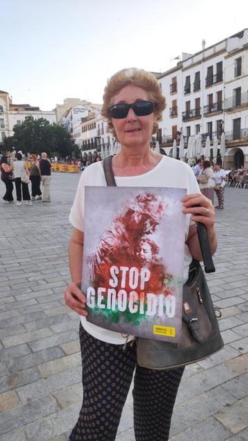 Una mujer, en la Plaza Mayor de Cáceres, sosteniendo un cartel con el lema STOP GENOCIDIO.