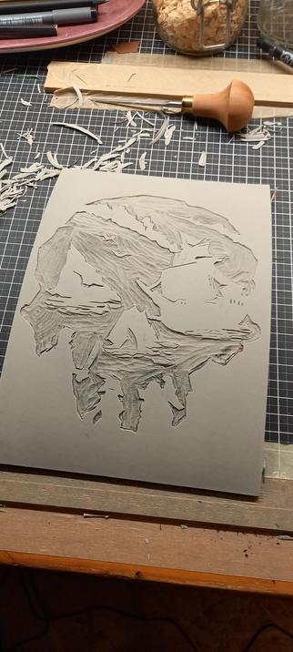 A cut linoleum printing sheet. Mirror image of the 'Sea of Thieves' video game logo. The view from inside a cave looking out, representing a skull like image.