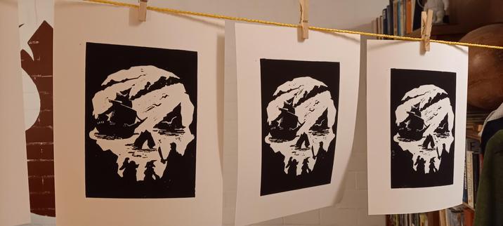 Printed image of the 'Sea of Thieves' video game logo. The view from inside a cave looking out, representing a skull like image.
3 sheets of paper hanging on a line to dry.