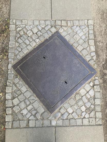 A square, simple cover arranged diagonally in a square section of the sidewalk 