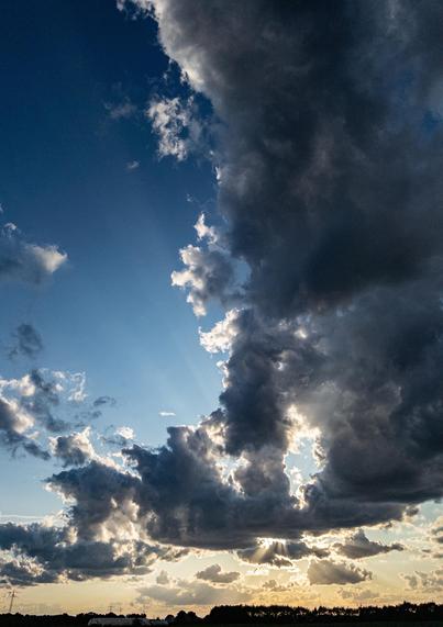 Looking northwest near sunset, across the flat Rhine valley near Ladenburg. The right hand side of the picture has some dark clouds, while the left is mostly blue. The sun is behind clouds closer to the horizon, and is making crepuscular rays in several directions.