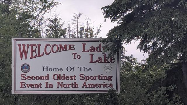 A large sign in a heavily wooded area that says: Welcome to Lady Lake, Home of the Second Oldest Sporting Event in North America.
(There is no indication what the event might be...)